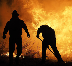 Schwarze Silouhetten zweier Personen vor Feuerwand. 