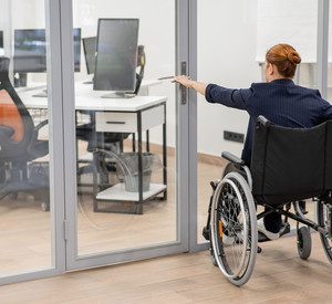 Red-haired caucasian woman in a wheelchair trying to open the door in the office.