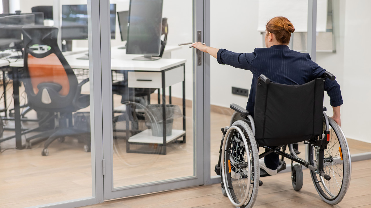 Red-haired caucasian woman in a wheelchair trying to open the door in the office.