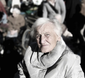 ältere Dame schaut in die Kamera, im Hintergrund verschwommen weitere ältere Menschen