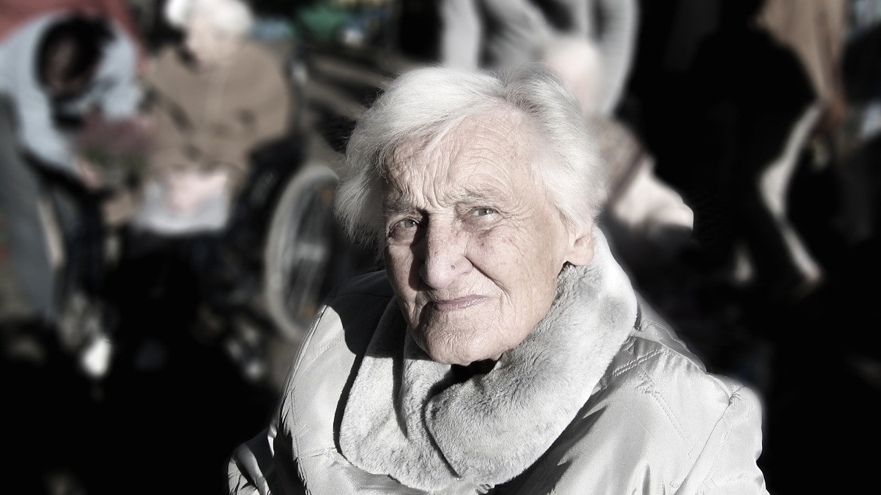 ältere Dame schaut in die Kamera, im Hintergrund verschwommen weitere ältere Menschen