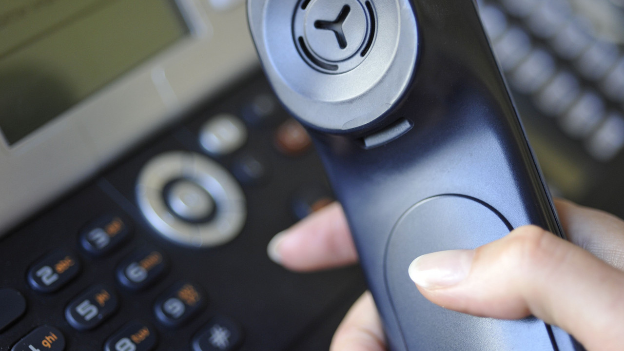 Hand hält schwarzen Telefonhörer.